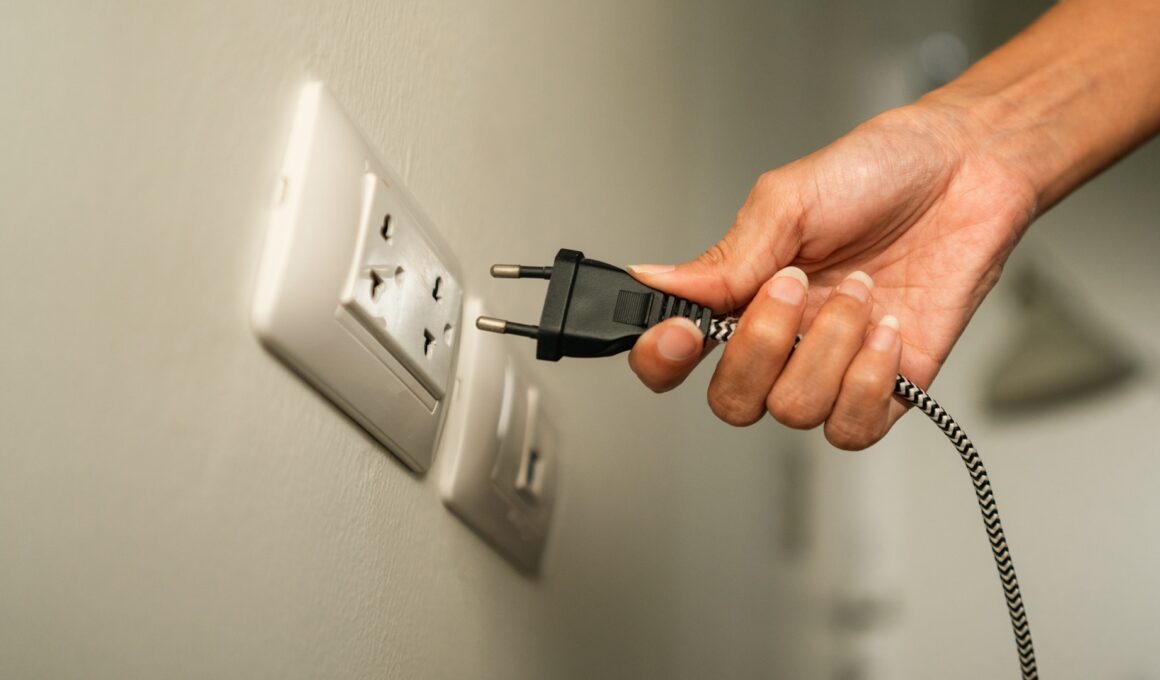 A hand holds a plug near a wall electrical outlet.