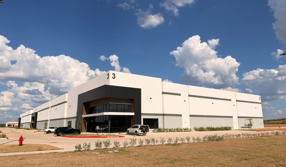 A white warehouse stands against a partly cloudy sky.